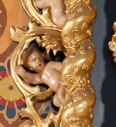 Zdjęcie nr 10: Nastawa ołtarzowa architektoniczna, jednoosiowa, jednokondygnacyjna ze zwieńczeniem. Ołtarz sarkofagowy, wybrzuszony w górnej części, zwężający się ku dołowi, na cokole; mensa drewniana. Na frontowej ścianie skrzyni ołtarzowej płycina w formie odwróconego trapezu. Nastawa ustawiona na dwustrefowym cokole, z wyłamanymi dwoma prostopadłościanami, ujęta parą kolumn o kręconych trzonach oplecionych wicią roślinną, dźwigających fragmenty gzymsu wyłamane pod kątem o wklęsłych bokach. Na nich ustawione figury dwóch aniołów. Niemal całe pole główne wypełnione jest wnęką w formie stojącego prostokąta o wklęsłych górnych narożach, z uskokiem, ujętą grubą, profilowaną ramą dekorowaną kwiatami, z obrazem Matki Boskiej Różańcowej. Pod wnęką płycina wypełniona kwiatami. Kondygnacja flankowana uszami utworzonymi z suchego akantu z dwiema parami puttów. Zwieńczenie w formie medalionu z obrazem Zwiastowania ujętego suchym akantem, zakończone cokołem z figurą anioła. Struktura polichromowana w kolorze niebieskim; kolumny, profile i ornamentyka złocone. 