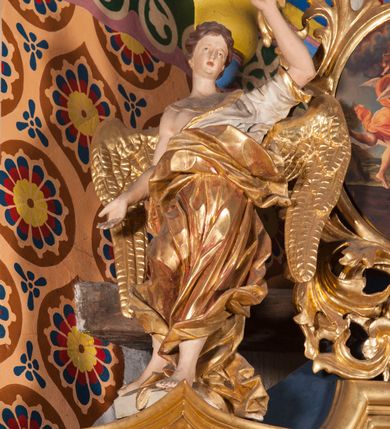 Zdjęcie nr 4: Nastawa ołtarzowa architektoniczna, jednoosiowa, jednokondygnacyjna ze zwieńczeniem. Ołtarz sarkofagowy, wybrzuszony w górnej części, zwężający się ku dołowi, na cokole; mensa drewniana. Na frontowej ścianie skrzyni ołtarzowej płycina w formie odwróconego trapezu. Nastawa ustawiona na dwustrefowym cokole, z wyłamanymi dwoma prostopadłościanami, ujęta parą kolumn o kręconych trzonach oplecionych wicią roślinną, dźwigających fragmenty gzymsu wyłamane pod kątem o wklęsłych bokach. Na nich ustawione figury dwóch aniołów. Niemal całe pole główne wypełnione jest wnęką w formie stojącego prostokąta o wklęsłych górnych narożach, z uskokiem, ujętą grubą, profilowaną ramą dekorowaną kwiatami, z obrazem Matki Boskiej Różańcowej. Pod wnęką płycina wypełniona kwiatami. Kondygnacja flankowana uszami utworzonymi z suchego akantu z dwiema parami puttów. Zwieńczenie w formie medalionu z obrazem Zwiastowania ujętego suchym akantem, zakończone cokołem z figurą anioła. Struktura polichromowana w kolorze niebieskim; kolumny, profile i ornamentyka złocone. 