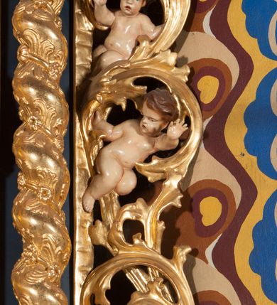 Zdjęcie nr 11: Nastawa ołtarzowa architektoniczna, jednoosiowa, jednokondygnacyjna ze zwieńczeniem. Ołtarz sarkofagowy, wybrzuszony w górnej części, zwężający się ku dołowi, na cokole; mensa drewniana. Na frontowej ścianie skrzyni ołtarzowej płycina w formie odwróconego trapezu. Nastawa ustawiona na dwustrefowym cokole, z wyłamanymi dwoma prostopadłościanami, ujęta parą kolumn o kręconych trzonach oplecionych wicią roślinną, dźwigających fragmenty gzymsu wyłamane pod kątem o wklęsłych bokach. Na nich ustawione figury dwóch aniołów. Niemal całe pole główne wypełnione jest wnęką w formie stojącego prostokąta o wklęsłych górnych narożach, z uskokiem, ujętą grubą, profilowaną ramą dekorowaną kwiatami, z obrazem Matki Boskiej Różańcowej. Pod wnęką płycina wypełniona kwiatami. Kondygnacja flankowana uszami utworzonymi z suchego akantu z dwiema parami puttów. Zwieńczenie w formie medalionu z obrazem Zwiastowania ujętego suchym akantem, zakończone cokołem z figurą anioła. Struktura polichromowana w kolorze niebieskim; kolumny, profile i ornamentyka złocone. 