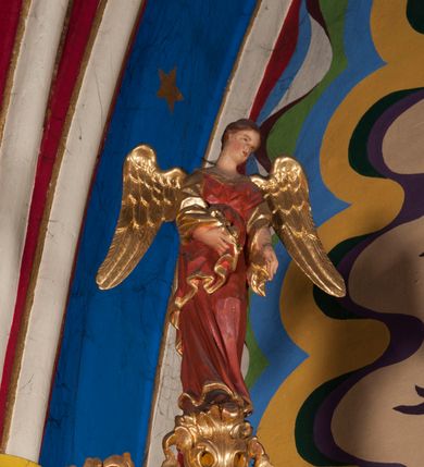 Zdjęcie nr 6: Nastawa ołtarzowa architektoniczna, jednoosiowa, jednokondygnacyjna ze zwieńczeniem. Ołtarz sarkofagowy, wybrzuszony w górnej części, zwężający się ku dołowi, na cokole; mensa drewniana. Na frontowej ścianie skrzyni ołtarzowej płycina w formie odwróconego trapezu. Nastawa ustawiona na dwustrefowym cokole, z wyłamanymi dwoma prostopadłościanami, ujęta parą kolumn o kręconych trzonach oplecionych wicią roślinną, dźwigających fragmenty gzymsu wyłamane pod kątem o wklęsłych bokach. Na nich ustawione figury dwóch aniołów. Niemal całe pole główne wypełnione jest wnęką w formie stojącego prostokąta o wklęsłych górnych narożach, z uskokiem, ujętą grubą, profilowaną ramą dekorowaną kwiatami, z obrazem Matki Boskiej Różańcowej. Pod wnęką płycina wypełniona kwiatami. Kondygnacja flankowana uszami utworzonymi z suchego akantu z dwiema parami puttów. Zwieńczenie w formie medalionu z obrazem Zwiastowania ujętego suchym akantem, zakończone cokołem z figurą anioła. Struktura polichromowana w kolorze niebieskim; kolumny, profile i ornamentyka złocone. 