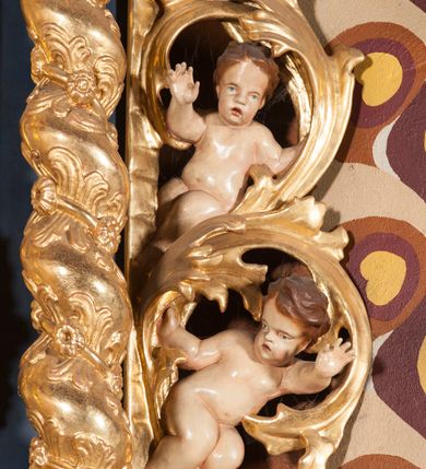 Zdjęcie nr 12: Nastawa ołtarzowa architektoniczna, jednoosiowa, jednokondygnacyjna ze zwieńczeniem. Ołtarz sarkofagowy, wybrzuszony w górnej części, zwężający się ku dołowi, na cokole; mensa drewniana. Na frontowej ścianie skrzyni ołtarzowej płycina w formie odwróconego trapezu. Nastawa ustawiona na dwustrefowym cokole, z wyłamanymi dwoma prostopadłościanami, ujęta parą kolumn o kręconych trzonach oplecionych wicią roślinną, dźwigających fragmenty gzymsu wyłamane pod kątem o wklęsłych bokach. Na nich ustawione figury dwóch aniołów. Niemal całe pole główne wypełnione jest wnęką w formie stojącego prostokąta o wklęsłych górnych narożach, z uskokiem, ujętą grubą, profilowaną ramą dekorowaną kwiatami, z obrazem Matki Boskiej Różańcowej. Pod wnęką płycina wypełniona kwiatami. Kondygnacja flankowana uszami utworzonymi z suchego akantu z dwiema parami puttów. Zwieńczenie w formie medalionu z obrazem Zwiastowania ujętego suchym akantem, zakończone cokołem z figurą anioła. Struktura polichromowana w kolorze niebieskim; kolumny, profile i ornamentyka złocone. 