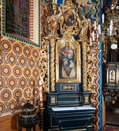 Zdjęcie nr 7: Nastawa ołtarzowa architektoniczna, jednoosiowa, jednokondygnacyjna ze zwieńczeniem. Ołtarz sarkofagowy, wybrzuszony w górnej części, zwężający się ku dołowi, na cokole; mensa drewniana. Na frontowej ścianie skrzyni ołtarzowej płycina w formie odwróconego trapezu. Nastawa ustawiona na dwustrefowym cokole, z wyłamanymi dwoma prostopadłościanami, ujęta parą kolumn o kręconych trzonach oplecionych wicią roślinną, dźwigających fragmenty gzymsu wyłamane pod kątem o wklęsłych bokach. Na nich ustawione figury dwóch aniołów. Niemal całe pole główne wypełnione jest wnęką w formie stojącego prostokąta o wklęsłych górnych narożach, z uskokiem, ujętą grubą, profilowaną ramą dekorowaną kwiatami, z obrazem Matki Boskiej Różańcowej. Pod wnęką płycina wypełniona kwiatami. Kondygnacja flankowana uszami utworzonymi z suchego akantu z dwiema parami puttów. Zwieńczenie w formie medalionu z obrazem Zwiastowania ujętego suchym akantem, zakończone cokołem z figurą anioła. Struktura polichromowana w kolorze niebieskim; kolumny, profile i ornamentyka złocone. 