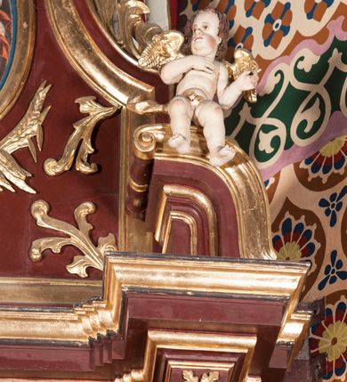 Zdjęcie nr 8: Nastawa architektoniczna, jednoosiowa, jednokondygnacyjna ze zwieńczeniem, ustawiona na dwustrefowym cokole z wyodrębnionymi dwoma prostopadłościanami. Ołtarz sarkofagowy, wybrzuszony w górnej części i zwężający się ku dołowi, na cokole; mensa drewniana. Na frontowej ścianie skrzyni ołtarzowej płycina w formie odwróconego trapezu dekorowana malowaną winną latoroślą na brązowo-zielonym tle. Na ołtarzu tabernakulum w formie drewnianej skrzynki, o ściętych narożach, ustawione na profilowanym cokole, zamknięte gzymsem. Ścianki dekorowane płycinami. Drzwiczki w formie stojącego prostokąta zamkniętego łukiem półkolistym nadwieszonym, z przedstawieniem kielicha z hostią. Nastawa ujęta parą kolumn dźwigających pełne belkowanie wyłamane na ich osi, z fryzem dekorowanym rozetami i kartuszem oraz fragmenty przerwanego półkolistego przyczółka z figurami puttów. Niemal całe pole środkowe wypełnione jest wnęką w formie stojącego prostokąta, ujętego grubą ramą dekorowaną rozetami, z obrazem Najświętszego Serca Jezusa. Zwieńczenie w formie zbliżonej do trapezu, o wklęsłych bokach, zamknięte wolutami i muszlą. W polu obraz Zwiastowania w formie stojącego owalu, ujęty profilowaną ramą, dekorowany naokoło ornamentem roślinnym. Struktura polichromowana w kolorze brązowo-czerwonym; kolumny, profile i ornamentyka złocone. 