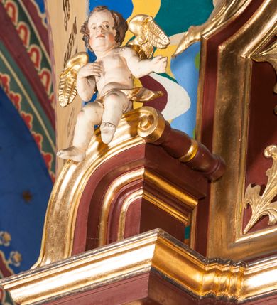 Zdjęcie nr 7: Nastawa architektoniczna, jednoosiowa, jednokondygnacyjna ze zwieńczeniem, ustawiona na dwustrefowym cokole z wyodrębnionymi dwoma prostopadłościanami. Ołtarz sarkofagowy, wybrzuszony w górnej części i zwężający się ku dołowi, na cokole; mensa drewniana. Na frontowej ścianie skrzyni ołtarzowej płycina w formie odwróconego trapezu dekorowana malowaną winną latoroślą na brązowo-zielonym tle. Na ołtarzu tabernakulum w formie drewnianej skrzynki, o ściętych narożach, ustawione na profilowanym cokole, zamknięte gzymsem. Ścianki dekorowane płycinami. Drzwiczki w formie stojącego prostokąta zamkniętego łukiem półkolistym nadwieszonym, z przedstawieniem kielicha z hostią. Nastawa ujęta parą kolumn dźwigających pełne belkowanie wyłamane na ich osi, z fryzem dekorowanym rozetami i kartuszem oraz fragmenty przerwanego półkolistego przyczółka z figurami puttów. Niemal całe pole środkowe wypełnione jest wnęką w formie stojącego prostokąta, ujętego grubą ramą dekorowaną rozetami, z obrazem Najświętszego Serca Jezusa. Zwieńczenie w formie zbliżonej do trapezu, o wklęsłych bokach, zamknięte wolutami i muszlą. W polu obraz Zwiastowania w formie stojącego owalu, ujęty profilowaną ramą, dekorowany naokoło ornamentem roślinnym. Struktura polichromowana w kolorze brązowo-czerwonym; kolumny, profile i ornamentyka złocone. 