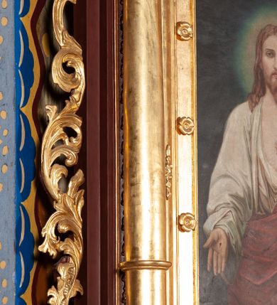 Zdjęcie nr 3: Obraz w formie stojącego prostokąta. W centrum Chrystus ukazany do kolan, frontalnie, lewą ręką odsłania szatę z piersi, prawą wyciąga do przodu, w geście otwartej dłoni. Twarz ma pociągłą, o dużych oczach, długim nosie i pełnych ustach, okoloną krótką, rozdwajającą się brodą oraz jasnymi włosami opadającymi na ramiona. Wokół głowy nimb. Ubrany jest w białą, luźną tunikę, odsłaniającą tors oraz czerwony płaszcz przewiązany diagonalnie przez lewe ramię i otaczający postać. Na jego piersi unosi się gorejące serce w glorii promienistej. Na dłoniach ma ślady męki. Chrystus ukazany jest na cieniowanym zielono-granatowym tle. Obraz ujęty złoconą, szeroką ramą, dekorowaną rzeźbionymi rozetami. 
