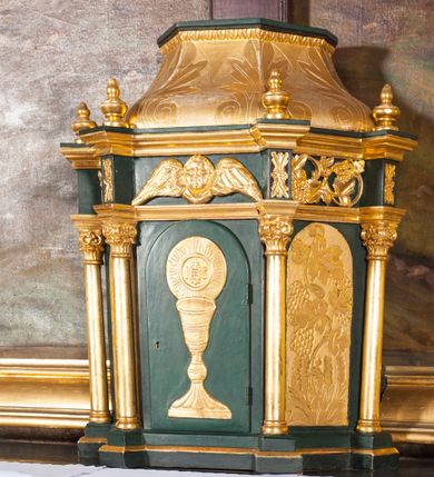 Zdjęcie nr 5: Nastawa niearchitektoniczna, ramowa, ustawiona na wysokim cokole. Ołtarz sarkofagowy, wybrzuszony w górnej części, zwężający się ku dołowi, na cokole; mensa drewniana. Na frontowej ścianie skrzyni ołtarzowej płycina w formie odwróconego trapezu dekorowana malowaną winną latoroślą na ciemnoczerwonym tle. Na ołtarzu ustawione tabernakulum w formie drewnianej skrzynki na planie połowy ośmioboku, wydzielone kolumienkami na cokołach, dźwigającymi pełne belkowanie o fryzie dekorowanym uskrzydloną główką anielską i ornamentem roślinnym. Na ściankach płyciny w kształcie stojącego prostokąta zamkniętego łukiem półkolistym wypełnione rytym ornamentem roślinnym. Drzwiczki o tej samej formie z rytym przedstawieniem kielicha z hostią w glorii. Tabernakulum zwieńczone tronem wystawienia w kształcie wklęsło-wypukłego cokołu, zwężającego się ku górze. Nastawa w formie stojącego prostokąta o wciętych górnych narożach, ujęta profilowaną ramą, z uszakami w formie spływów wolutowych z wyodrębnionymi zwojami dekorowanymi ornamentem roślinnym; zwieńczona rocaille'owym kartuszem. W polu figura Chrystusa Ukrzyżowanego przybita do prostego krzyża, ukazanego na tle malowanej panoramy Jerozolimy, w której prawym dolnym roku znajduje się sygnatura „S(tanisław) Karas / 1913”. 



