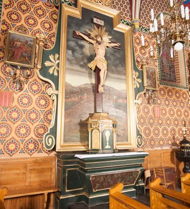 Zdjęcie nr 2: Nastawa niearchitektoniczna, ramowa, ustawiona na wysokim cokole. Ołtarz sarkofagowy, wybrzuszony w górnej części, zwężający się ku dołowi, na cokole; mensa drewniana. Na frontowej ścianie skrzyni ołtarzowej płycina w formie odwróconego trapezu dekorowana malowaną winną latoroślą na ciemnoczerwonym tle. Na ołtarzu ustawione tabernakulum w formie drewnianej skrzynki na planie połowy ośmioboku, wydzielone kolumienkami na cokołach, dźwigającymi pełne belkowanie o fryzie dekorowanym uskrzydloną główką anielską i ornamentem roślinnym. Na ściankach płyciny w kształcie stojącego prostokąta zamkniętego łukiem półkolistym wypełnione rytym ornamentem roślinnym. Drzwiczki o tej samej formie z rytym przedstawieniem kielicha z hostią w glorii. Tabernakulum zwieńczone tronem wystawienia w kształcie wklęsło-wypukłego cokołu, zwężającego się ku górze. Nastawa w formie stojącego prostokąta o wciętych górnych narożach, ujęta profilowaną ramą, z uszakami w formie spływów wolutowych z wyodrębnionymi zwojami dekorowanymi ornamentem roślinnym; zwieńczona rocaille&#039;owym kartuszem. W polu figura Chrystusa Ukrzyżowanego przybita do prostego krzyża, ukazanego na tle malowanej panoramy Jerozolimy, w której prawym dolnym roku znajduje się sygnatura „S(tanisław) Karas / 1913”. 



