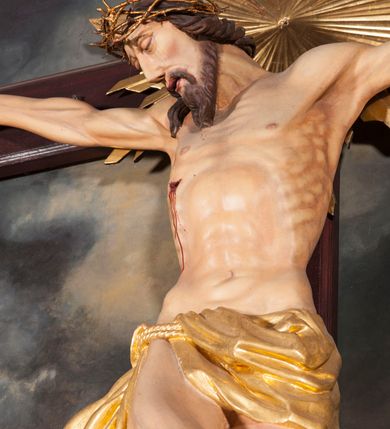 Zdjęcie nr 4: Figura Chrystusa umarłego przybita jest trzema gwoździami do krzyża o prostych ramionach. Ciało w lekkim zwisie o horyzontalnie rozłożonych ramionach, z głową opadającą na prawy bark, nogi silnie ugięte w kolanach, stopy skrzyżowane w układzie prawa na lewą. Chrystus ma podłużną twarz, o migdałowatych, zamkniętych oczach, dużym, garbatym nosie oraz szerokich, rozchylonych ustach, okoloną krótką brodą oraz skręconymi w pukle włosami opadającymi na prawe ramię. Na głowie ma nałożoną koronę cierniową. Ciało ma silnie wychudzone z wyraźnie podkreślonymi guzowatymi żebrami, mostkiem i kośćmi biodrowymi, z silnie wciętą talią oraz zapadłą płaszczyzną brzucha. Nogi i ręce o podkreślonej wklęsło-wypukłej linii mięśni i ścięgien. Złocone perizonium zawieszone na podwójnym sznurze, odsłaniające prawe udo, z rozwianym zwisem tkaniny na prawym boku. Na krzyżowaniu belek krzyża, na tle głowy Zbawiciela gloria promienista. Na zakończeniu pionowej belki krzyża banderola z napisem „IN RI”. Polichromia ciała Chrystusa naturalistyczna, z zaznaczonymi śladami męki. 


