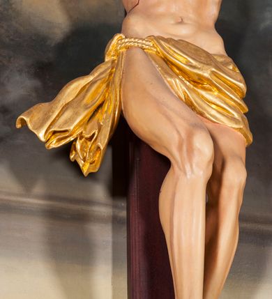 Zdjęcie nr 6: Figura Chrystusa umarłego przybita jest trzema gwoździami do krzyża o prostych ramionach. Ciało w lekkim zwisie o horyzontalnie rozłożonych ramionach, z głową opadającą na prawy bark, nogi silnie ugięte w kolanach, stopy skrzyżowane w układzie prawa na lewą. Chrystus ma podłużną twarz, o migdałowatych, zamkniętych oczach, dużym, garbatym nosie oraz szerokich, rozchylonych ustach, okoloną krótką brodą oraz skręconymi w pukle włosami opadającymi na prawe ramię. Na głowie ma nałożoną koronę cierniową. Ciało ma silnie wychudzone z wyraźnie podkreślonymi guzowatymi żebrami, mostkiem i kośćmi biodrowymi, z silnie wciętą talią oraz zapadłą płaszczyzną brzucha. Nogi i ręce o podkreślonej wklęsło-wypukłej linii mięśni i ścięgien. Złocone perizonium zawieszone na podwójnym sznurze, odsłaniające prawe udo, z rozwianym zwisem tkaniny na prawym boku. Na krzyżowaniu belek krzyża, na tle głowy Zbawiciela gloria promienista. Na zakończeniu pionowej belki krzyża banderola z napisem „IN RI”. Polichromia ciała Chrystusa naturalistyczna, z zaznaczonymi śladami męki. 


