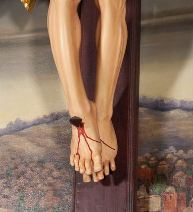 Zdjęcie nr 8: Figura Chrystusa umarłego przybita jest trzema gwoździami do krzyża o prostych ramionach. Ciało w lekkim zwisie o horyzontalnie rozłożonych ramionach, z głową opadającą na prawy bark, nogi silnie ugięte w kolanach, stopy skrzyżowane w układzie prawa na lewą. Chrystus ma podłużną twarz, o migdałowatych, zamkniętych oczach, dużym, garbatym nosie oraz szerokich, rozchylonych ustach, okoloną krótką brodą oraz skręconymi w pukle włosami opadającymi na prawe ramię. Na głowie ma nałożoną koronę cierniową. Ciało ma silnie wychudzone z wyraźnie podkreślonymi guzowatymi żebrami, mostkiem i kośćmi biodrowymi, z silnie wciętą talią oraz zapadłą płaszczyzną brzucha. Nogi i ręce o podkreślonej wklęsło-wypukłej linii mięśni i ścięgien. Złocone perizonium zawieszone na podwójnym sznurze, odsłaniające prawe udo, z rozwianym zwisem tkaniny na prawym boku. Na krzyżowaniu belek krzyża, na tle głowy Zbawiciela gloria promienista. Na zakończeniu pionowej belki krzyża banderola z napisem „IN RI”. Polichromia ciała Chrystusa naturalistyczna, z zaznaczonymi śladami męki. 


