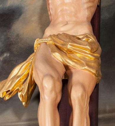 Zdjęcie nr 5: Figura Chrystusa umarłego przybita jest trzema gwoździami do krzyża o prostych ramionach. Ciało w lekkim zwisie o horyzontalnie rozłożonych ramionach, z głową opadającą na prawy bark, nogi silnie ugięte w kolanach, stopy skrzyżowane w układzie prawa na lewą. Chrystus ma podłużną twarz, o migdałowatych, zamkniętych oczach, dużym, garbatym nosie oraz szerokich, rozchylonych ustach, okoloną krótką brodą oraz skręconymi w pukle włosami opadającymi na prawe ramię. Na głowie ma nałożoną koronę cierniową. Ciało ma silnie wychudzone z wyraźnie podkreślonymi guzowatymi żebrami, mostkiem i kośćmi biodrowymi, z silnie wciętą talią oraz zapadłą płaszczyzną brzucha. Nogi i ręce o podkreślonej wklęsło-wypukłej linii mięśni i ścięgien. Złocone perizonium zawieszone na podwójnym sznurze, odsłaniające prawe udo, z rozwianym zwisem tkaniny na prawym boku. Na krzyżowaniu belek krzyża, na tle głowy Zbawiciela gloria promienista. Na zakończeniu pionowej belki krzyża banderola z napisem „IN RI”. Polichromia ciała Chrystusa naturalistyczna, z zaznaczonymi śladami męki. 


