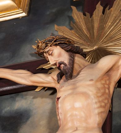 Zdjęcie nr 2: Figura Chrystusa umarłego przybita jest trzema gwoździami do krzyża o prostych ramionach. Ciało w lekkim zwisie o horyzontalnie rozłożonych ramionach, z głową opadającą na prawy bark, nogi silnie ugięte w kolanach, stopy skrzyżowane w układzie prawa na lewą. Chrystus ma podłużną twarz, o migdałowatych, zamkniętych oczach, dużym, garbatym nosie oraz szerokich, rozchylonych ustach, okoloną krótką brodą oraz skręconymi w pukle włosami opadającymi na prawe ramię. Na głowie ma nałożoną koronę cierniową. Ciało ma silnie wychudzone z wyraźnie podkreślonymi guzowatymi żebrami, mostkiem i kośćmi biodrowymi, z silnie wciętą talią oraz zapadłą płaszczyzną brzucha. Nogi i ręce o podkreślonej wklęsło-wypukłej linii mięśni i ścięgien. Złocone perizonium zawieszone na podwójnym sznurze, odsłaniające prawe udo, z rozwianym zwisem tkaniny na prawym boku. Na krzyżowaniu belek krzyża, na tle głowy Zbawiciela gloria promienista. Na zakończeniu pionowej belki krzyża banderola z napisem „IN RI”. Polichromia ciała Chrystusa naturalistyczna, z zaznaczonymi śladami męki. 


