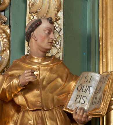 Zdjęcie nr 2: Rzeźba z tyłu drążona, ukazana frontalnie z głową skierowaną w prawo, w kontrapoście, o esowato wygiętej sylwetce. Jej prawa ręka jest zgięta, uniesiona, w lewej trzyma otwartą księgę z napisem: „SI QUAERIS MIRACULA”. Postać ma owalną twarz, o indywidualnych rysach, podwójnym podbródku, głęboko osadzonych, półprzymkniętych oczach, małym nosie, drobnych, wąskich ustach. Okalają ją krótkie włosy w postaci loków, z tonsurą na czubku głowy. Postać ubrana w habit przewiązany sznurem w talii oraz pelerynę. Tkanina delikatnie marszczona, dołem drapowana w długie pojedyncze fałdy, miejscami ściśle przylegająca do ciała. Polichromia naturalistyczna w partiach ciała, szaty pozłacane, atrybuty posrebrzane.