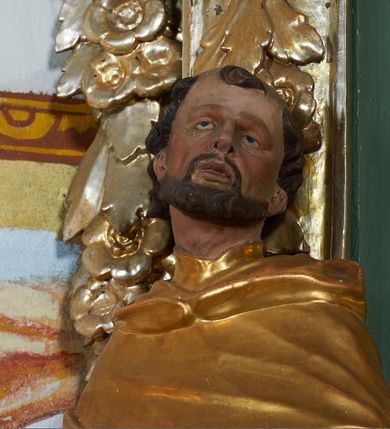 Zdjęcie nr 6: Rzeźba drążona z tyłu, ukazana frontalnie z głową skierowaną w prawo, w kontrapoście, o esowato wygiętej sylwetce. Lewa ręka świętego podtrzymuje księgę opartą na biodrze, prawa jest zgięta i uniesiona w bok. Twarz pociągła, o długim nosie, półprzymkniętych oczach zwróconych ku górze. Okolona jest krótką brodą oraz włosami z tonsurą na czubku głowy. Święty ubrany jest w habit oraz płaszcz zawinięty na prawej nodze. Habit o delikatnych załamaniach tkaniny, ściśle przylegający do ciała. Płaszcz głęboko rzeźbiony, silnie marszczony o grubych, ostrych fałdach. Polichromia naturalistyczna w partiach ciała, szaty złocone, atrybuty srebrzone.