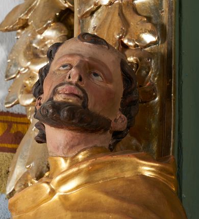 Zdjęcie nr 7: Rzeźba drążona z tyłu, ukazana frontalnie z głową skierowaną w prawo, w kontrapoście, o esowato wygiętej sylwetce. Lewa ręka świętego podtrzymuje księgę opartą na biodrze, prawa jest zgięta i uniesiona w bok. Twarz pociągła, o długim nosie, półprzymkniętych oczach zwróconych ku górze. Okolona jest krótką brodą oraz włosami z tonsurą na czubku głowy. Święty ubrany jest w habit oraz płaszcz zawinięty na prawej nodze. Habit o delikatnych załamaniach tkaniny, ściśle przylegający do ciała. Płaszcz głęboko rzeźbiony, silnie marszczony o grubych, ostrych fałdach. Polichromia naturalistyczna w partiach ciała, szaty złocone, atrybuty srebrzone.