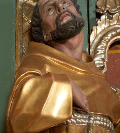 Zdjęcie nr 4: Rzeźba drążona z tyłu, zwrócona w trzech czwartych w prawo z głową odchyloną w tył, zwróconą w górę, stoi w kontrapoście, sylwetka esowato wygięta. W uniesionej lewej ręce święty trzyma zawiniętą kartę z napisem „PEREUNT PERICULA”, prawa ugięta, dłonią wskazuje na pierś. Twarz pociągła, szczupła, o dużych oczach skierowanych ku górze, długim nosie, delikatnie rozchylonych ustach. Okolona jest krótką brodą oraz krótkimi włosami, delikatnie falowanymi z tonsurą na czubku głowy. Święty jest ubrany w habit, przewiązany w talii podwójnym sznurem ze zwisem z trzema guzami. Polichromia naturalistyczna w partiach ciała, szaty pozłacane, atrybuty posrebrzane.