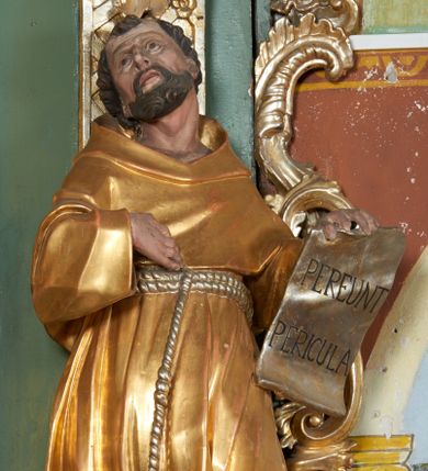 Zdjęcie nr 1: Rzeźba drążona z tyłu, zwrócona w trzech czwartych w prawo z głową odchyloną w tył, zwróconą w górę, stoi w kontrapoście, sylwetka esowato wygięta. W uniesionej lewej ręce święty trzyma zawiniętą kartę z napisem „PEREUNT PERICULA”, prawa ugięta, dłonią wskazuje na pierś. Twarz pociągła, szczupła, o dużych oczach skierowanych ku górze, długim nosie, delikatnie rozchylonych ustach. Okolona jest krótką brodą oraz krótkimi włosami, delikatnie falowanymi z tonsurą na czubku głowy. Święty jest ubrany w habit, przewiązany w talii podwójnym sznurem ze zwisem z trzema guzami. Polichromia naturalistyczna w partiach ciała, szaty pozłacane, atrybuty posrebrzane.