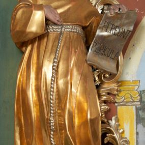 Zdjęcie nr 1: Rzeźba drążona z tyłu, zwrócona w trzech czwartych w prawo z głową odchyloną w tył, zwróconą w górę, stoi w kontrapoście, sylwetka esowato wygięta. W uniesionej lewej ręce święty trzyma zawiniętą kartę z napisem „PEREUNT PERICULA”, prawa ugięta, dłonią wskazuje na pierś. Twarz pociągła, szczupła, o dużych oczach skierowanych ku górze, długim nosie, delikatnie rozchylonych ustach. Okolona jest krótką brodą oraz krótkimi włosami, delikatnie falowanymi z tonsurą na czubku głowy. Święty jest ubrany w habit, przewiązany w talii podwójnym sznurem ze zwisem z trzema guzami. Polichromia naturalistyczna w partiach ciała, szaty pozłacane, atrybuty posrebrzane.