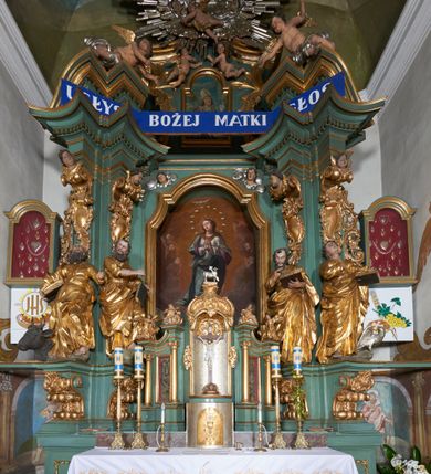 Zdjęcie nr 4: Rzeźba drążona z tyłu, ukazana frontalnie, w wykroku, z głową przechyloną delikatnie w tył, skierowaną w lewo. Prawa ręka ugięta, dłonią wskazuje na pierś, lewą święty przytrzymuje na biodrze zamkniętą księgę. Twarz ma podłużną, pełną, o młodzieńczych rysach, długim nosie, głęboko osadzonych i otwartych oczach zwróconych ku górze oraz delikatnie rozchylonych ustach. Włosy w postaci loków opadają na plecy. Święty ubrany w ściśle przylegającą do ciała tunikę przewiązaną w talii oraz otaczający postać płaszcz zawieszony na lewym ramieniu. Tunika delikatnie marszczona, ściśle przylegająca do ciała, zaś draperia płaszcza głęboko rzeźbiona, ekspresyjnie fałdowana. Przy lewej nodze postaci figura orła. Polichromia naturalistyczna w partiach ciała, szaty pozłacane, orzeł posrebrzany.