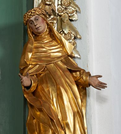 Zdjęcie nr 1: Rzeźba drążona z tyłu, ukazana frontalnie, z pochyloną głową i przechyloną w prawo sylwetką, obie ręce rozłożone na boki. Jej twarz jest okrągła, o głęboko osadzonych oczach skierowanych w dół, dużym nosie i delikatnie rozchylonych ustach. Święta jest ubrana w habit, płaszcz oraz welon z koroną cierniową na głowie. Tkanina sztywna, delikatnie łamana, płaszcz ekspresyjnie drapowany w grube fałdy. Polichromia w partiach ciała naturalistyczna, szaty pozłacane.