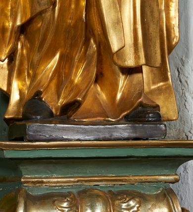 Zdjęcie nr 7: Rzeźba drążona z tyłu, ukazana frontalnie, z pochyloną głową i przechyloną w prawo sylwetką, obie ręce rozłożone na boki. Jej twarz jest okrągła, o głęboko osadzonych oczach skierowanych w dół, dużym nosie i delikatnie rozchylonych ustach. Święta jest ubrana w habit, płaszcz oraz welon z koroną cierniową na głowie. Tkanina sztywna, delikatnie łamana, płaszcz ekspresyjnie drapowany w grube fałdy. Polichromia w partiach ciała naturalistyczna, szaty pozłacane.