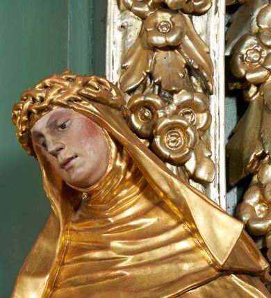 Zdjęcie nr 4: Rzeźba drążona z tyłu, ukazana frontalnie, z pochyloną głową i przechyloną w prawo sylwetką, obie ręce rozłożone na boki. Jej twarz jest okrągła, o głęboko osadzonych oczach skierowanych w dół, dużym nosie i delikatnie rozchylonych ustach. Święta jest ubrana w habit, płaszcz oraz welon z koroną cierniową na głowie. Tkanina sztywna, delikatnie łamana, płaszcz ekspresyjnie drapowany w grube fałdy. Polichromia w partiach ciała naturalistyczna, szaty pozłacane.