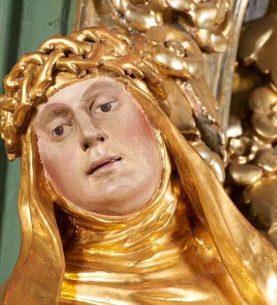 Zdjęcie nr 5: Rzeźba drążona z tyłu, ukazana frontalnie, z pochyloną głową i przechyloną w prawo sylwetką, obie ręce rozłożone na boki. Jej twarz jest okrągła, o głęboko osadzonych oczach skierowanych w dół, dużym nosie i delikatnie rozchylonych ustach. Święta jest ubrana w habit, płaszcz oraz welon z koroną cierniową na głowie. Tkanina sztywna, delikatnie łamana, płaszcz ekspresyjnie drapowany w grube fałdy. Polichromia w partiach ciała naturalistyczna, szaty pozłacane.