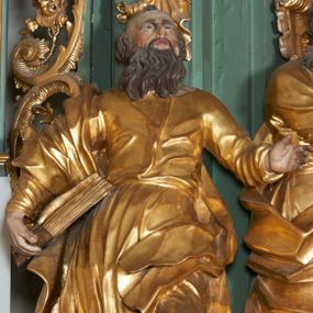 Zdjęcie nr 1: Rzeźba drążona z tyłu, zwrócona frontalnie, z głową skierowaną ku górze, o esowato wygiętej sylwetce, w kontrapoście, z lewą nogą opartą na skale. Lewa ręka jest ugięta i uniesiona, prawą święty przytrzymuje księgę, opierając ją na biodrze. Twarz ma pociągłą, o starczych rysach, długim nosie, delikatnie rozchylonych ustach i oczach zwróconych w górę. Okolona jest długą brodą w formie opadających na pierś pukli. Włosy ma krótkie. Postać ubrana jest w przylegającą do ciała tunikę, delikatnie marszczoną w partii torsu i obficie fałdowaną u spodu oraz przewiązany diagonalnie płaszcz, zawieszony na prawym ramieniu, opadający na lewe biodro w postaci silnie giętej i obficie marszczonej tkaniny. Przy prawej stopie postaci głowa wołu. Polichromia naturalistyczna w partiach ciała i atrybutów, szaty pozłacane.