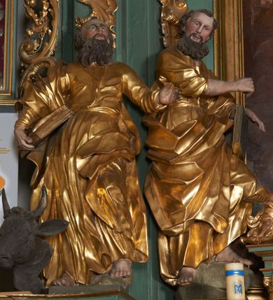 Zdjęcie nr 1: Rzeźba drążona z tyłu, zwrócona w trzech czwartych w lewo, z głową skierowaną w prawo, lewa noga silnie ugięta, oparta na skale. Prawa ręka jest uniesiona na wysokości piersi, lewa podtrzymuje księgę opartą na udzie. Twarz podłużna, o niewielkich oczach, dużym nosie i delikatnie rozchylonych ustach okolona długą brodą skręconą w dwa pukle opadające na pierś oraz krótkimi włosami. Postać jest ubrana w tunikę silnie przylegającą w partii torsu, przepasaną w talii sznurem, spływającą w postaci głęboko rzeźbionych, sztywnych fałd. Płaszcz przewiązany diagonalnie, zawinięty na prawym biodrze w formie ekspresyjnie fałdowanej, grubej tkaniny. Przy lewej nodze głowa lwa. Polichromia w partiach ciała naturalistyczna, szaty złocone.