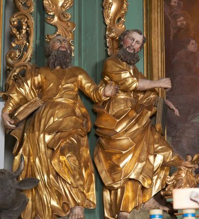 Zdjęcie nr 2: Rzeźba drążona z tyłu, zwrócona w trzech czwartych w lewo, z głową skierowaną w prawo, lewa noga silnie ugięta, oparta na skale. Prawa ręka jest uniesiona na wysokości piersi, lewa podtrzymuje księgę opartą na udzie. Twarz podłużna, o niewielkich oczach, dużym nosie i delikatnie rozchylonych ustach okolona długą brodą skręconą w dwa pukle opadające na pierś oraz krótkimi włosami. Postać jest ubrana w tunikę silnie przylegającą w partii torsu, przepasaną w talii sznurem, spływającą w postaci głęboko rzeźbionych, sztywnych fałd. Płaszcz przewiązany diagonalnie, zawinięty na prawym biodrze w formie ekspresyjnie fałdowanej, grubej tkaniny. Przy lewej nodze głowa lwa. Polichromia w partiach ciała naturalistyczna, szaty złocone.