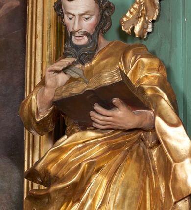 Zdjęcie nr 2: Rzeźba drążona z tyłu, zwrócona frontalnie z pochyloną głową, w kontrapoście, o esowato wygiętej sylwetce. Lewa ręka postaci ugięta podtrzymuje księgę na wysokości piersi, w prawej, uniesionej święty trzyma pióro. Twarz podłużna, zindywidualizowana, o długim nosie, oczach zwróconych w dół i delikatnie rozchylonych ustach; okolona długą brodą spływającą na pierś. Włosy krótkie, w postaci loków. Tunika ściśle przylegająca do ciała i delikatnie marszczona. Płaszcz przewieszony diagonalnie przez lewe ramię i zawieszony na prawym biodrze, w postaci ekspresyjnie rzeźbionej, obficie fałdowanej, ciężkiej tkaniny. Partie ciała i atrybuty polichromowane naturalistycznie, szaty złocone.