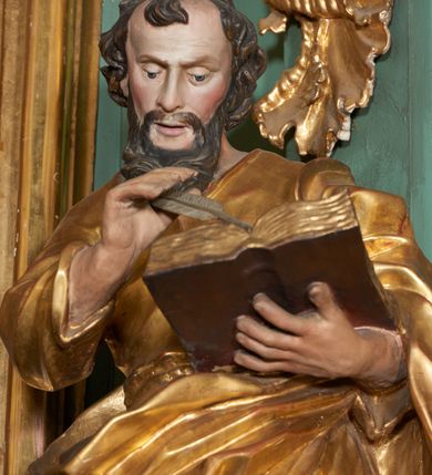 Zdjęcie nr 3: Rzeźba drążona z tyłu, zwrócona frontalnie z pochyloną głową, w kontrapoście, o esowato wygiętej sylwetce. Lewa ręka postaci ugięta podtrzymuje księgę na wysokości piersi, w prawej, uniesionej święty trzyma pióro. Twarz podłużna, zindywidualizowana, o długim nosie, oczach zwróconych w dół i delikatnie rozchylonych ustach; okolona długą brodą spływającą na pierś. Włosy krótkie, w postaci loków. Tunika ściśle przylegająca do ciała i delikatnie marszczona. Płaszcz przewieszony diagonalnie przez lewe ramię i zawieszony na prawym biodrze, w postaci ekspresyjnie rzeźbionej, obficie fałdowanej, ciężkiej tkaniny. Partie ciała i atrybuty polichromowane naturalistycznie, szaty złocone.