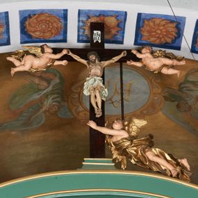 Zdjęcie nr 1: Belka tęczowa w formie łuku segmentowego nadwieszonego z krucyfiksem umieszczonym na środku, na profilowanym cokole. Do prostego krzyża przybita trzema gwoździami figura umarłego Chrystusa. Postać ukazana w lekkim zwisie, o szeroko rozłożonych ramionach, z głową opadającą na prawy bark, nogi lekko ugięte w kolanach. Twarz Chrystusa jest pociągła, szczupła, o głęboko osadzonych, zamkniętych oczach, długim, wąskim nosie i niewielkich ustach, okolona jest zarostem i długimi włosami w postaci wijących się pukli, opadających na plecy i ramiona. Na głowie korona cierniowa. Ciało o wyraźnie podkreślonej anatomii klatki piersiowej oraz muskulaturze ramion i nóg. Perizonium sięgające połowy ud, obficie fałdowane, zawiązane na lewym boku ze zwisem tkaniny. Ramiona poziomej belki krzyża podtrzymują małe, uskrzydlone aniołki, przepasane złotą tkaniną, zaś pionową, u spodu podtrzymuje nadlatujący anioł przedstawiony w pozycji półleżącej w silnie rozwianych i głęboko sfałdowanych szatach. Karnacja Chrystusa i aniołów malowana farbą olejną w kolorach naturalnych, perizonium białe, skrzydła i szaty aniołów pozłacane.