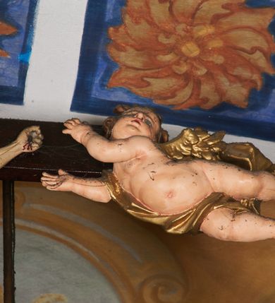 Zdjęcie nr 8: Belka tęczowa w formie łuku segmentowego nadwieszonego z krucyfiksem umieszczonym na środku, na profilowanym cokole. Do prostego krzyża przybita trzema gwoździami figura umarłego Chrystusa. Postać ukazana w lekkim zwisie, o szeroko rozłożonych ramionach, z głową opadającą na prawy bark, nogi lekko ugięte w kolanach. Twarz Chrystusa jest pociągła, szczupła, o głęboko osadzonych, zamkniętych oczach, długim, wąskim nosie i niewielkich ustach, okolona jest zarostem i długimi włosami w postaci wijących się pukli, opadających na plecy i ramiona. Na głowie korona cierniowa. Ciało o wyraźnie podkreślonej anatomii klatki piersiowej oraz muskulaturze ramion i nóg. Perizonium sięgające połowy ud, obficie fałdowane, zawiązane na lewym boku ze zwisem tkaniny. Ramiona poziomej belki krzyża podtrzymują małe, uskrzydlone aniołki, przepasane złotą tkaniną, zaś pionową, u spodu podtrzymuje nadlatujący anioł przedstawiony w pozycji półleżącej w silnie rozwianych i głęboko sfałdowanych szatach. Karnacja Chrystusa i aniołów malowana farbą olejną w kolorach naturalnych, perizonium białe, skrzydła i szaty aniołów pozłacane.