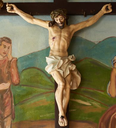 Zdjęcie nr 1: Figura umarłego Chrystusa przybita trzema gwoździami do krzyża o prostych ramionach. Ciało w lekkim zwisie, o szeroko rozłożonych ramionach, układających się w delikatny łuk, esowato wygiętej sylwetce, głowa opada bezwładnie na prawy bark, obie nogi ugięte w kolanach, stopy skrzyżowane w układzie prawa na lewą. Twarz trójkątna, szczupła, o zamkniętych oczach, dużym, prostym nosie i wąskich ustach, okolona krótką brodą i włosami silnie skręconymi w pukle. Na głowie szeroka, zielona korona cierniowa. Ciało wychudzone, o silnie podkreślonej muskulaturze oraz żebrach klatki piersiowej. Biodra przepasane białym, krótkim i silnie drapowanym perizonium, zawiązanym na lewym boku. Polichromia ciała naturalistyczna z zaznaczonymi śladami męki. Na zakończeniu pionowej belki krzyża banderola z napisem „I.N./R.I.”