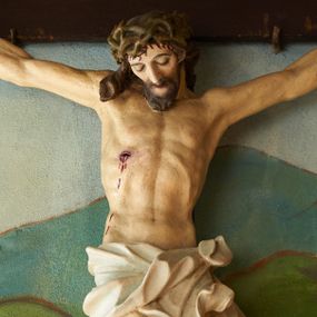 Zdjęcie nr 1: Figura umarłego Chrystusa przybita trzema gwoździami do krzyża o prostych ramionach. Ciało w lekkim zwisie, o szeroko rozłożonych ramionach, układających się w delikatny łuk, esowato wygiętej sylwetce, głowa opada bezwładnie na prawy bark, obie nogi ugięte w kolanach, stopy skrzyżowane w układzie prawa na lewą. Twarz trójkątna, szczupła, o zamkniętych oczach, dużym, prostym nosie i wąskich ustach, okolona krótką brodą i włosami silnie skręconymi w pukle. Na głowie szeroka, zielona korona cierniowa. Ciało wychudzone, o silnie podkreślonej muskulaturze oraz żebrach klatki piersiowej. Biodra przepasane białym, krótkim i silnie drapowanym perizonium, zawiązanym na lewym boku. Polichromia ciała naturalistyczna z zaznaczonymi śladami męki. Na zakończeniu pionowej belki krzyża banderola z napisem „I.N./R.I.”