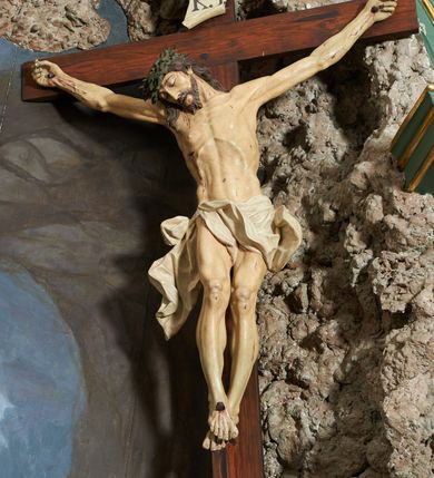 Zdjęcie nr 2: Krzyż zwrócony jest w trzech czwartych w lewo, lekko pochylony, na górnej belce krzyża zwój z napisem „I.N / R.I.”. Do niego przybita jest trzema gwoździami pełnoplastyczna rzeźba umarłego Chrystusa. Figura w delikatnym zwisie ciała o szeroko rozłożonych ramionach oraz łukowato wygiętej sylwetce, głowa opada bezwładnie na prawy bark, nogi lekko ugięte w kolanach, stopy skrzyżowane w układzie prawa na lewą. Twarz o łagodnych rysach, zamkniętych oczach, długim, prostym nosie oraz nieznacznie rozchylonych ustach, okolona krótką brodą. Włosy rzeźbione w silnie skręcone pukle opadające na ramię i plecy, na głowie korona cierniowa. Ciało silnie wychudzone z zaznaczonymi śladami męki, plastycznie modelowane, o wyraźnie podkreślonej muskulaturze ramion i ud oraz żeber klatki piersiowej. Perizonium w formie ekspresyjnie rozwianej, silnie drapowanej tkaniny, przewiązanej podwójnym sznurem, odsłaniającej prawe biodro, z obfitym zwisem na prawym biodrze. Polichromia naturalistyczna, karnacja bladobeżowa, włosy ciemnobrązowe, perizonium białe.