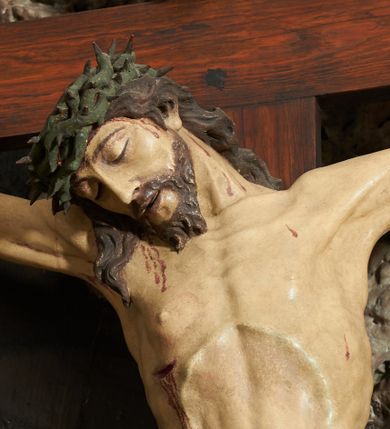 Zdjęcie nr 4: Krzyż zwrócony jest w trzech czwartych w lewo, lekko pochylony, na górnej belce krzyża zwój z napisem „I.N / R.I.”. Do niego przybita jest trzema gwoździami pełnoplastyczna rzeźba umarłego Chrystusa. Figura w delikatnym zwisie ciała o szeroko rozłożonych ramionach oraz łukowato wygiętej sylwetce, głowa opada bezwładnie na prawy bark, nogi lekko ugięte w kolanach, stopy skrzyżowane w układzie prawa na lewą. Twarz o łagodnych rysach, zamkniętych oczach, długim, prostym nosie oraz nieznacznie rozchylonych ustach, okolona krótką brodą. Włosy rzeźbione w silnie skręcone pukle opadające na ramię i plecy, na głowie korona cierniowa. Ciało silnie wychudzone z zaznaczonymi śladami męki, plastycznie modelowane, o wyraźnie podkreślonej muskulaturze ramion i ud oraz żeber klatki piersiowej. Perizonium w formie ekspresyjnie rozwianej, silnie drapowanej tkaniny, przewiązanej podwójnym sznurem, odsłaniającej prawe biodro, z obfitym zwisem na prawym biodrze. Polichromia naturalistyczna, karnacja bladobeżowa, włosy ciemnobrązowe, perizonium białe.
