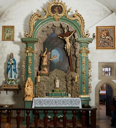 Zdjęcie nr 6: Krzyż zwrócony jest w trzech czwartych w lewo, lekko pochylony, na górnej belce krzyża zwój z napisem „I.N / R.I.”. Do niego przybita jest trzema gwoździami pełnoplastyczna rzeźba umarłego Chrystusa. Figura w delikatnym zwisie ciała o szeroko rozłożonych ramionach oraz łukowato wygiętej sylwetce, głowa opada bezwładnie na prawy bark, nogi lekko ugięte w kolanach, stopy skrzyżowane w układzie prawa na lewą. Twarz o łagodnych rysach, zamkniętych oczach, długim, prostym nosie oraz nieznacznie rozchylonych ustach, okolona krótką brodą. Włosy rzeźbione w silnie skręcone pukle opadające na ramię i plecy, na głowie korona cierniowa. Ciało silnie wychudzone z zaznaczonymi śladami męki, plastycznie modelowane, o wyraźnie podkreślonej muskulaturze ramion i ud oraz żeber klatki piersiowej. Perizonium w formie ekspresyjnie rozwianej, silnie drapowanej tkaniny, przewiązanej podwójnym sznurem, odsłaniającej prawe biodro, z obfitym zwisem na prawym biodrze. Polichromia naturalistyczna, karnacja bladobeżowa, włosy ciemnobrązowe, perizonium białe.