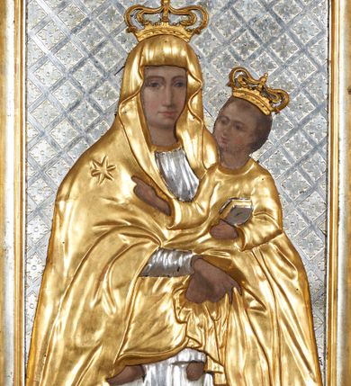 Zdjęcie nr 1: Obraz w formie stojącego prostokąta. Matka Boska ukazana w półpostaci, zwrócona frontalnie, na lewej ręce podtrzymuje Dzieciątko, prawą krzyżuje z przodu z dłonią w geście błogosławieństwa. Twarz o śniadej karnacji łagodnych rysach, z długim prostym nosem i ciemnobrązowymi oczami. Maria ubrana w posrebrzaną suknię z wąskimi rękawami oraz pozłacany maforion z gwiazdą na prawym ramieniu narzucony na głowę i ramiona. Dzieciątko zwrócone w trzech czwartych w lewo, lewą ręką trzyma przy boku zamkniętą księgę, prawą wykonuje gest błogosławieństwa. Twarz okrągła o śniadej karnacji z ciemnobrązowymi oczami, prostym nosem, pełnymi ustami, okolona krótkimi brązowymi włosami, układającymi się w lekko skręcone pukle. Dzieciątko jest ubrane w długą złotą tunikę z wąskimi rękawami. Na głowach obu postaci zamknięte złote korony. Postacie ukazane na tle posrebrzanej, płaskorzeźbionej kratki wypełnionej rozetami. Twarze, dłonie i stopy Marii i Jezusa malowane na drewnie, szaty i korony płaskorzeźbione. 