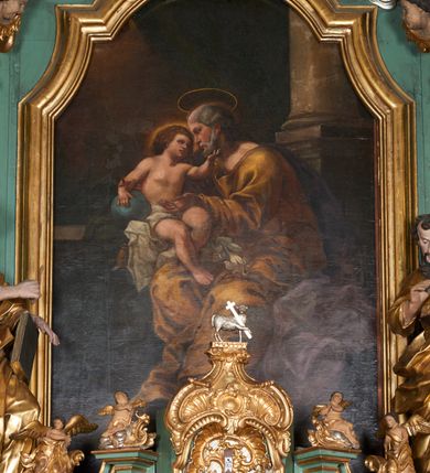 Zdjęcie nr 4: Obraz w formie stojącego prostokąta. W centrum postać siedzącego św. Józefa z Dzieciątkiem. Święty zwrócony jest w trzech czwartych w prawo, z głową ukazaną w profilu. Prawą ręką podtrzymuje siedzące obok Dzieciątko, lewą wyciąga przed siebie. Twarz ma pociągłą, o głęboko osadzonych oczach, okoloną siwym zarostem i włosami. Nad głową ma nimb. Święty ubrany jest w żółtą tunikę z dużym dekoltem, obficie drapowaną oraz fioletowy płaszcz spływający na plecy i opadający po lewej stronie postaci. Na jego kolanach leżą białe lilie. Dzieciątko siedzi na parapecie, na poduszce, w otoczeniu zielonej draperii, zwrócone jest w trzech czwartych w lewo, w stronę Józefa. Lewą dłonią ujmuje jego twarz, prawą trzyma przy boku kulę zwieńczoną krzyżem. Twarz ma pełną, z oczami skierowanymi ku górze, małym nosem i pełnymi ustami, okoloną gęstymi, brązowymi włosami. Wokół głowy jasna poświata. Dzieciątko w partii bioder przepasane jest białą, obficie drapowaną tkaniną. W prawej części obrazu fragment kolumny na postumencie, w lewej widoczny kamienny parapet. W głębi, za kolumną podwieszona jest zielona kotara. W lewym górnym rogu uskrzydlone główki anielskie pośród obłoków na rozświetlonym tle (zasłonięte przez ramę). Kolorystyka ciepła, brunatna, z dominantą żółcieni i brązów, przełamana zimnymi zieleniami i błękitami, silny światłocień.