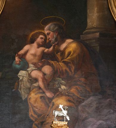 Zdjęcie nr 1: Obraz w formie stojącego prostokąta. W centrum postać siedzącego św. Józefa z Dzieciątkiem. Święty zwrócony jest w trzech czwartych w prawo, z głową ukazaną w profilu. Prawą ręką podtrzymuje siedzące obok Dzieciątko, lewą wyciąga przed siebie. Twarz ma pociągłą, o głęboko osadzonych oczach, okoloną siwym zarostem i włosami. Nad głową ma nimb. Święty ubrany jest w żółtą tunikę z dużym dekoltem, obficie drapowaną oraz fioletowy płaszcz spływający na plecy i opadający po lewej stronie postaci. Na jego kolanach leżą białe lilie. Dzieciątko siedzi na parapecie, na poduszce, w otoczeniu zielonej draperii, zwrócone jest w trzech czwartych w lewo, w stronę Józefa. Lewą dłonią ujmuje jego twarz, prawą trzyma przy boku kulę zwieńczoną krzyżem. Twarz ma pełną, z oczami skierowanymi ku górze, małym nosem i pełnymi ustami, okoloną gęstymi, brązowymi włosami. Wokół głowy jasna poświata. Dzieciątko w partii bioder przepasane jest białą, obficie drapowaną tkaniną. W prawej części obrazu fragment kolumny na postumencie, w lewej widoczny kamienny parapet. W głębi, za kolumną podwieszona jest zielona kotara. W lewym górnym rogu uskrzydlone główki anielskie pośród obłoków na rozświetlonym tle (zasłonięte przez ramę). Kolorystyka ciepła, brunatna, z dominantą żółcieni i brązów, przełamana zimnymi zieleniami i błękitami, silny światłocień.
