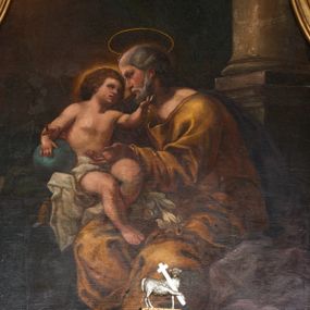 Zdjęcie nr 1: Obraz w formie stojącego prostokąta. W centrum postać siedzącego św. Józefa z Dzieciątkiem. Święty zwrócony jest w trzech czwartych w prawo, z głową ukazaną w profilu. Prawą ręką podtrzymuje siedzące obok Dzieciątko, lewą wyciąga przed siebie. Twarz ma pociągłą, o głęboko osadzonych oczach, okoloną siwym zarostem i włosami. Nad głową ma nimb. Święty ubrany jest w żółtą tunikę z dużym dekoltem, obficie drapowaną oraz fioletowy płaszcz spływający na plecy i opadający po lewej stronie postaci. Na jego kolanach leżą białe lilie. Dzieciątko siedzi na parapecie, na poduszce, w otoczeniu zielonej draperii, zwrócone jest w trzech czwartych w lewo, w stronę Józefa. Lewą dłonią ujmuje jego twarz, prawą trzyma przy boku kulę zwieńczoną krzyżem. Twarz ma pełną, z oczami skierowanymi ku górze, małym nosem i pełnymi ustami, okoloną gęstymi, brązowymi włosami. Wokół głowy jasna poświata. Dzieciątko w partii bioder przepasane jest białą, obficie drapowaną tkaniną. W prawej części obrazu fragment kolumny na postumencie, w lewej widoczny kamienny parapet. W głębi, za kolumną podwieszona jest zielona kotara. W lewym górnym rogu uskrzydlone główki anielskie pośród obłoków na rozświetlonym tle (zasłonięte przez ramę). Kolorystyka ciepła, brunatna, z dominantą żółcieni i brązów, przełamana zimnymi zieleniami i błękitami, silny światłocień.