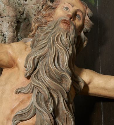 Zdjęcie nr 4: W polu ołtarza imitującego grotę skalną znajduje się figura św. Onufrego modlącego się przed krucyfiksem. Po lewej stronie pełnoplastyczna figura klęczącego świętego ukazanego z profilu, z uniesionymi wysoko obiema rękami i głową. Twarz o starczych rysach, zwróconych w górę oczach, dużym nosie i otwartych ustach z widocznym uzębieniem, okolona bardzo długą, siwą brodą w postaci falowanych pasm, sięgających ziemi. Włosy siwe, zmierzwione, opadają na plecy w formie długich skręconych pasm, sięgających stóp. Ciało szczupłe, plastyczne modelowane, o wyraźnie zarysowanej anatomii i starczych cechach. Biodra przepasane liściastą gałązką. 
Polichromia naturalistyczna.