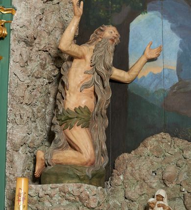 Zdjęcie nr 2: W polu ołtarza imitującego grotę skalną znajduje się figura św. Onufrego modlącego się przed krucyfiksem. Po lewej stronie pełnoplastyczna figura klęczącego świętego ukazanego z profilu, z uniesionymi wysoko obiema rękami i głową. Twarz o starczych rysach, zwróconych w górę oczach, dużym nosie i otwartych ustach z widocznym uzębieniem, okolona bardzo długą, siwą brodą w postaci falowanych pasm, sięgających ziemi. Włosy siwe, zmierzwione, opadają na plecy w formie długich skręconych pasm, sięgających stóp. Ciało szczupłe, plastyczne modelowane, o wyraźnie zarysowanej anatomii i starczych cechach. Biodra przepasane liściastą gałązką. 
Polichromia naturalistyczna.