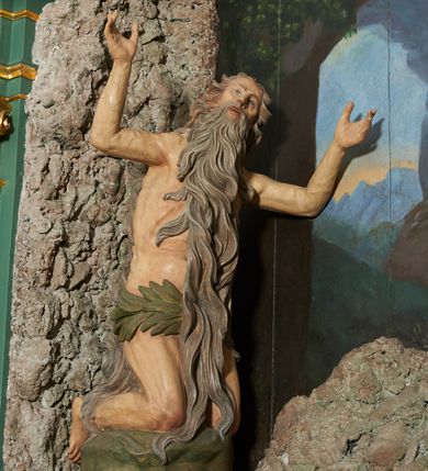 Zdjęcie nr 3: W polu ołtarza imitującego grotę skalną znajduje się figura św. Onufrego modlącego się przed krucyfiksem. Po lewej stronie pełnoplastyczna figura klęczącego świętego ukazanego z profilu, z uniesionymi wysoko obiema rękami i głową. Twarz o starczych rysach, zwróconych w górę oczach, dużym nosie i otwartych ustach z widocznym uzębieniem, okolona bardzo długą, siwą brodą w postaci falowanych pasm, sięgających ziemi. Włosy siwe, zmierzwione, opadają na plecy w formie długich skręconych pasm, sięgających stóp. Ciało szczupłe, plastyczne modelowane, o wyraźnie zarysowanej anatomii i starczych cechach. Biodra przepasane liściastą gałązką. 
Polichromia naturalistyczna.