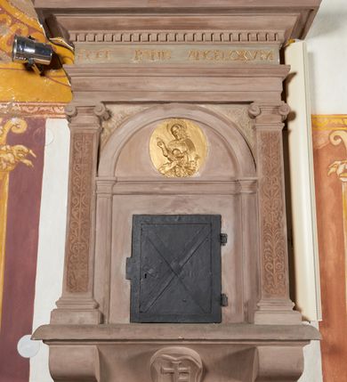Zdjęcie nr 2: Sakramentarium architektoniczne, w formie aediculi, na podstawie przyjmującej kształt parapetu podtrzymywanego przez dwie konsole, pomiędzy którymi w kartuszu znajduje się rzeźbiony herb Prus I. Flankowane jest pilastrami o głowicach jońskich i trzonach dekorowanych rytą groteską, dźwigającymi pełne belkowanie z silnie wysuniętym gzymsem dekorowanym kostkowaniem. Fryz ze złoconą inskrypcją „ECCE PANIS ANGELORVUM”. W polu głównym znajduje się półkolista arkada  wsparta na toskańskich pilastrach, podzielona gzymsem na dwie części, w dolnej znajdują się kute drzwiczki w formie stojącego prostokąta, w górnej, w tympanonie pozłacany, owalny medalion z płaskorzeźbioną półpostacią błogosławiącego Chrystusa trzymającego kulę zwieńczoną krzyżem. W przyłuczach arkady ryta arabeska. Sakramentarium polichromowane w kolorze blado różowym z pozłacanymi detalami.

