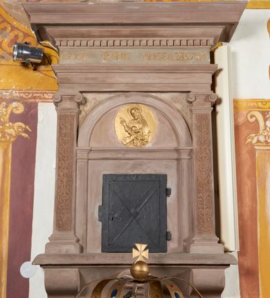 Zdjęcie nr 3: Sakramentarium architektoniczne, w formie aediculi, na podstawie przyjmującej kształt parapetu podtrzymywanego przez dwie konsole, pomiędzy którymi w kartuszu znajduje się rzeźbiony herb Prus I. Flankowane jest pilastrami o głowicach jońskich i trzonach dekorowanych rytą groteską, dźwigającymi pełne belkowanie z silnie wysuniętym gzymsem dekorowanym kostkowaniem. Fryz ze złoconą inskrypcją „ECCE PANIS ANGELORVUM”. W polu głównym znajduje się półkolista arkada  wsparta na toskańskich pilastrach, podzielona gzymsem na dwie części, w dolnej znajdują się kute drzwiczki w formie stojącego prostokąta, w górnej, w tympanonie pozłacany, owalny medalion z płaskorzeźbioną półpostacią błogosławiącego Chrystusa trzymającego kulę zwieńczoną krzyżem. W przyłuczach arkady ryta arabeska. Sakramentarium polichromowane w kolorze blado różowym z pozłacanymi detalami.

