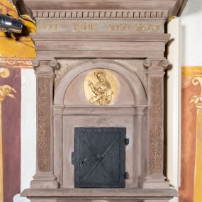 Zdjęcie nr 1: Sakramentarium architektoniczne, w formie aediculi, na podstawie przyjmującej kształt parapetu podtrzymywanego przez dwie konsole, pomiędzy którymi w kartuszu znajduje się rzeźbiony herb Prus I. Flankowane jest pilastrami o głowicach jońskich i trzonach dekorowanych rytą groteską, dźwigającymi pełne belkowanie z silnie wysuniętym gzymsem dekorowanym kostkowaniem. Fryz ze złoconą inskrypcją „ECCE PANIS ANGELORVUM”. W polu głównym znajduje się półkolista arkada  wsparta na toskańskich pilastrach, podzielona gzymsem na dwie części, w dolnej znajdują się kute drzwiczki w formie stojącego prostokąta, w górnej, w tympanonie pozłacany, owalny medalion z płaskorzeźbioną półpostacią błogosławiącego Chrystusa trzymającego kulę zwieńczoną krzyżem. W przyłuczach arkady ryta arabeska. Sakramentarium polichromowane w kolorze blado różowym z pozłacanymi detalami.

