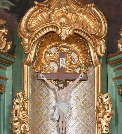 Zdjęcie nr 5: Tabernakulum w formie sześcianu, z wypukłym frontem. Drzwiczki w formie stojącego prostokąta zamkniętego łukiem półkolistym z aplikacją przedstawiającą kielich z hostią z monogramem IHS w glorii. Tron wystawienia architektoniczny, trójosiowy. Oś środkowa w postaci obrotowej niszy ujętej w profilowaną ramę, z konchą utworzoną z rocaille'u, zakończona ornamentalnym zwieńczeniem dekorowanym muszlą, małżowiną i kartuszem, które tworzą postument dla rzeźby baranka z krzyżem. Osie boczne na cokole, cofniętym pod kątem w tył, ujęte dwiema parami kolumn różnej wysokości o kapitelach kompozytowych, dźwigających pełne belkowanie w formie spływu, wyłamane w ich partii, na których znajdują się siedzące i klęczące figury aniołów. Między kolumnami prostokątne płyciny z wotami. Struktura polichromowana w kolorze jasnozielonym z pozłoconymi profilami i ornamentyką.